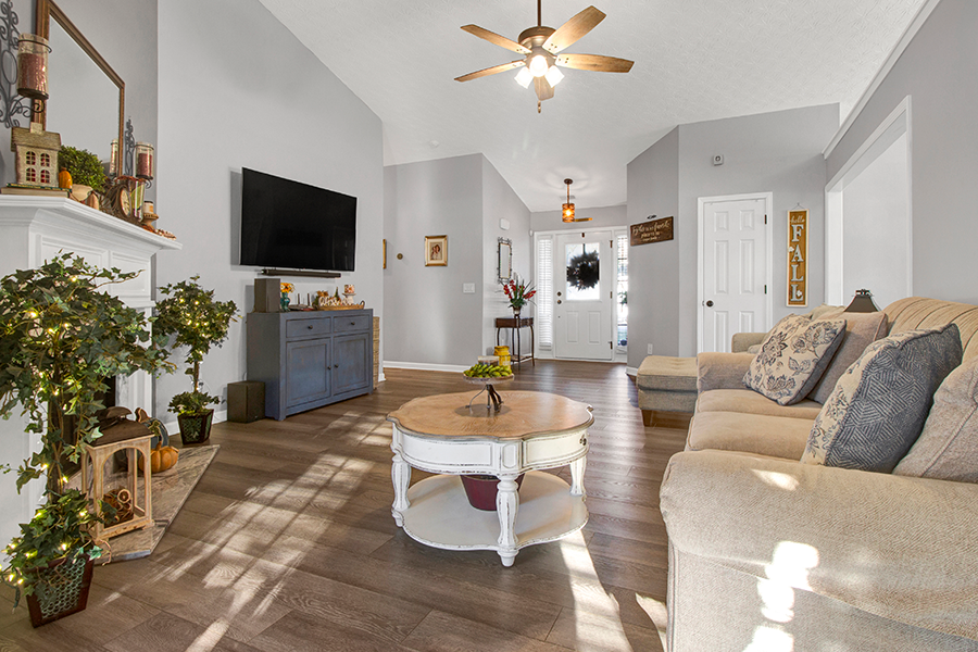 Modern living room with vaulted ceilings, neutral gray walls, wood flooring, and cozy decor, featuring a wall-mounted TV, fireplace, and natural lighting, perfect for open-concept home buyers in Acworth, Georgia